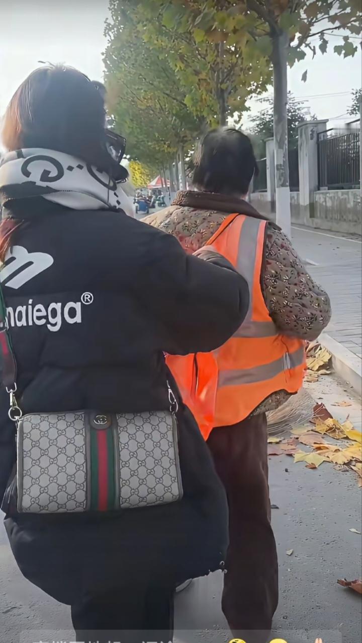 马路边的人行道上，一名环卫工阿姨，正在忙碌地清扫着地上的落叶。正走到这段路的一名