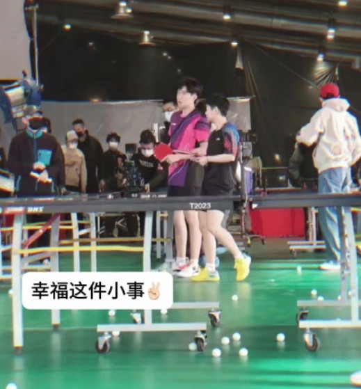 幸福这件小事～可口可乐广告拍摄现场。穿着同款黄色外套的王楚钦背靠背坐在长椅上，