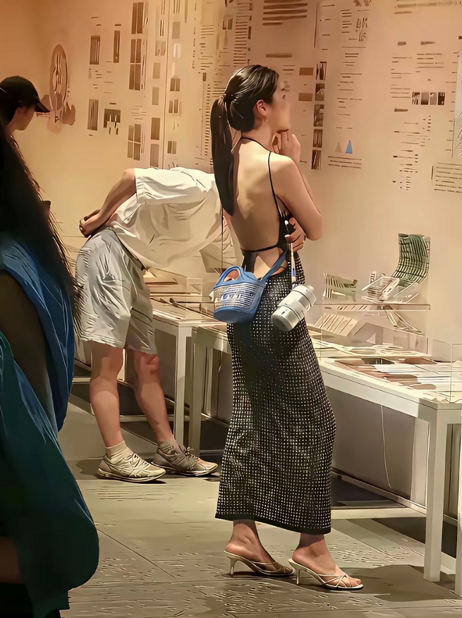 目瞪口呆！一位穿着清凉的年轻美女在博物馆认真欣赏着展品。她身穿一件露背黑白方格