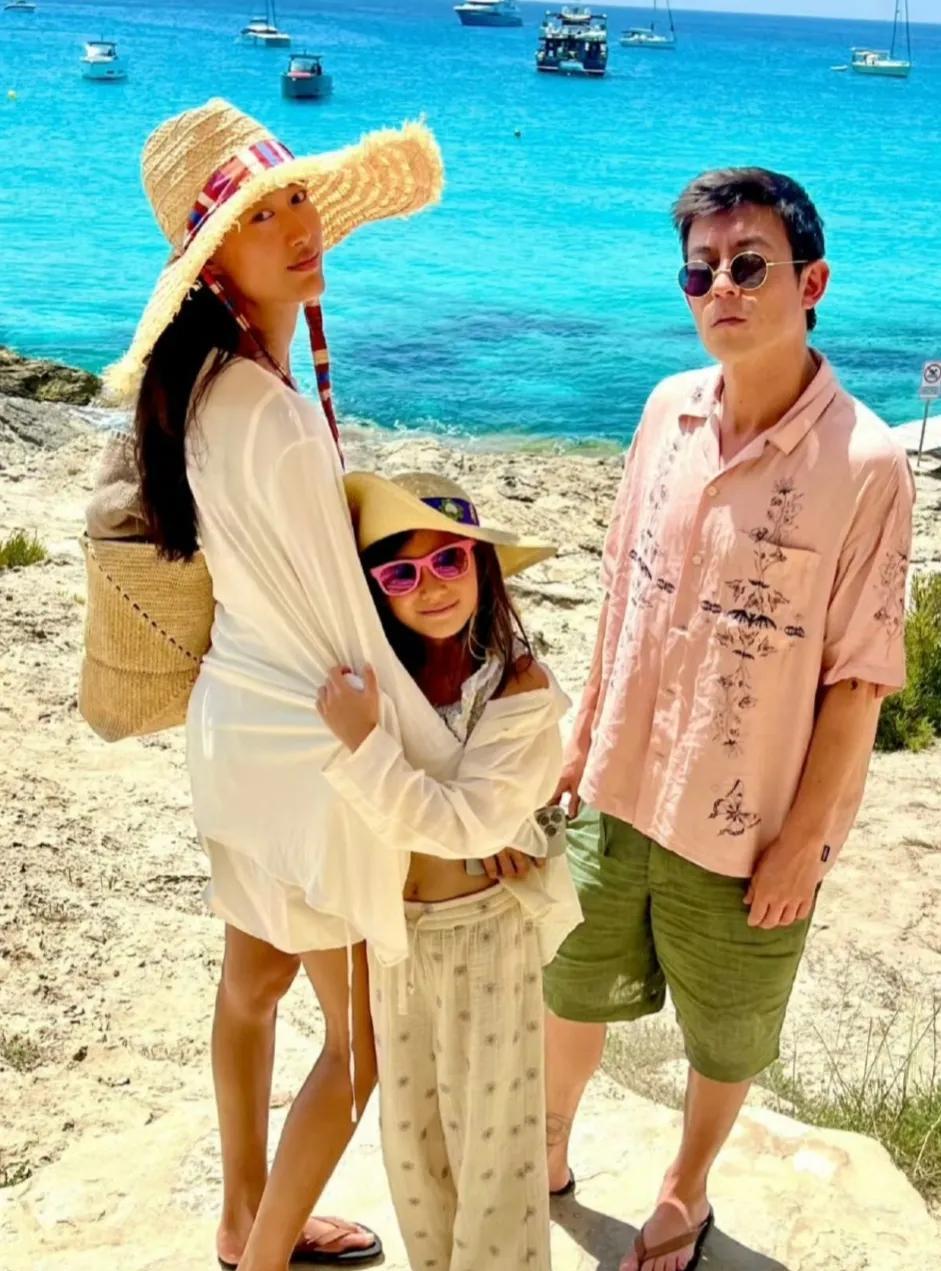 陈冠希陪老婆和女儿海边度假，陈冠希身穿粉色衬衫搭配绿色短裤，戴着墨镜仰着头站一边