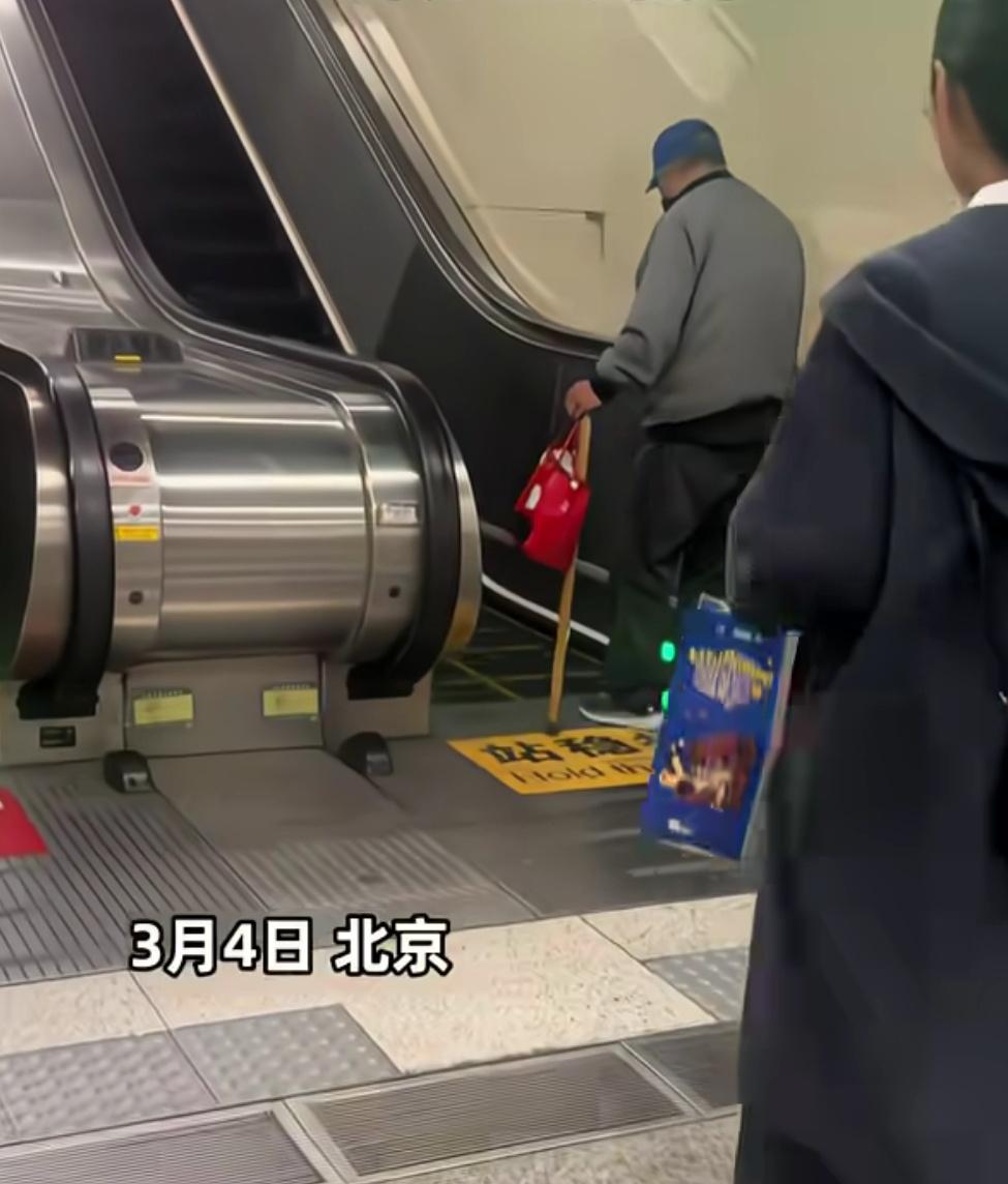 北京一老人行动不便站在扶梯前徘徊，后面乘客无人上前搀扶，全部在他身后耐心等待，连