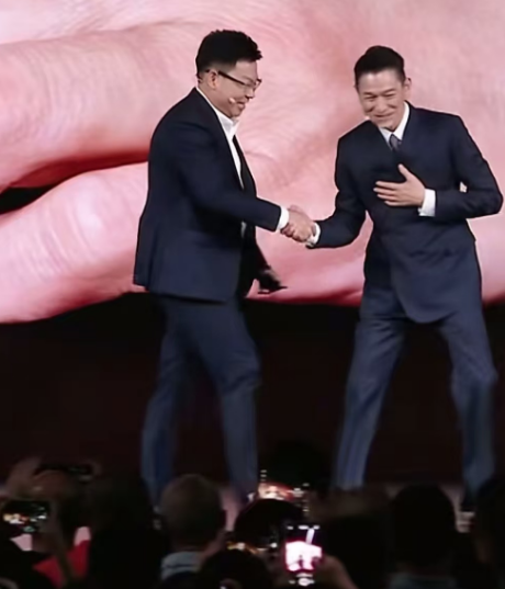 刘德华太懂人情世故了。当他看到华为的余承东走上台来，他主动迎上去，一只手放在