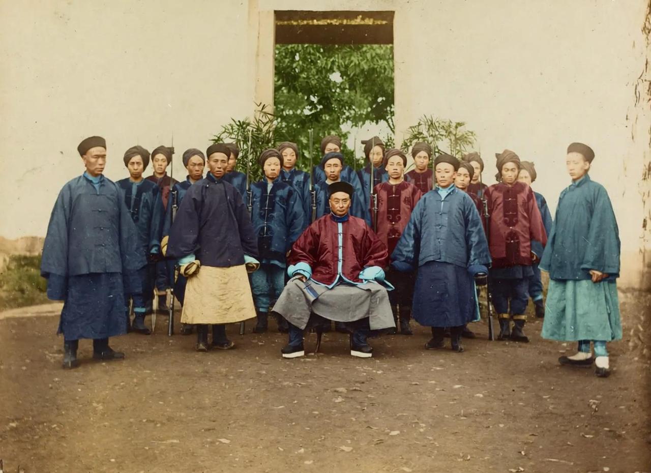 这张照片是清末重庆总兵章高元，周围站立的僚属穿传统长袍马褂，后方持长枪的卫队则裹