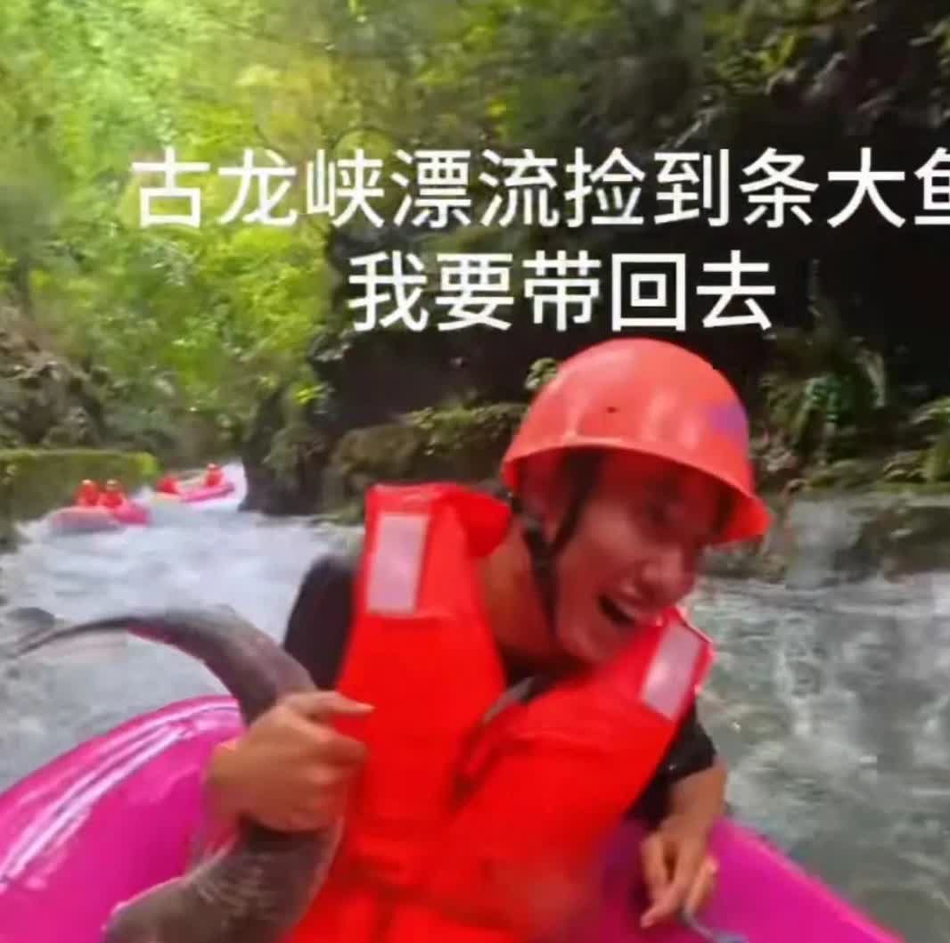 一男子与朋友在古龙峡漂流时，一条十几斤重的大鱼跳到漂流船里，被男子给抓住，男子笑