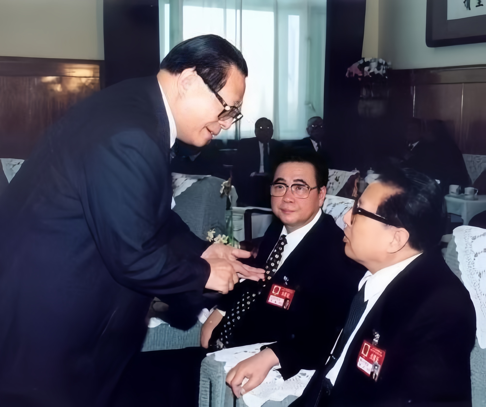 李鹏乔石坐着，而江同志站着弯下腰，打着手势和他们两位商量工作。三位都是正国级领导
