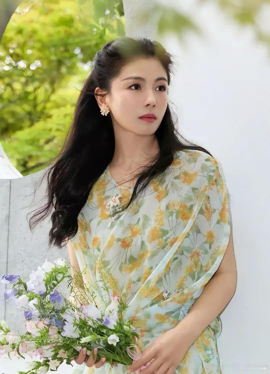 刘涛一袭浅绿印花薄纱长裙，清雅又灵动，庭院光影之下，手捧鲜花浅笑嫣然，松弛感拉满