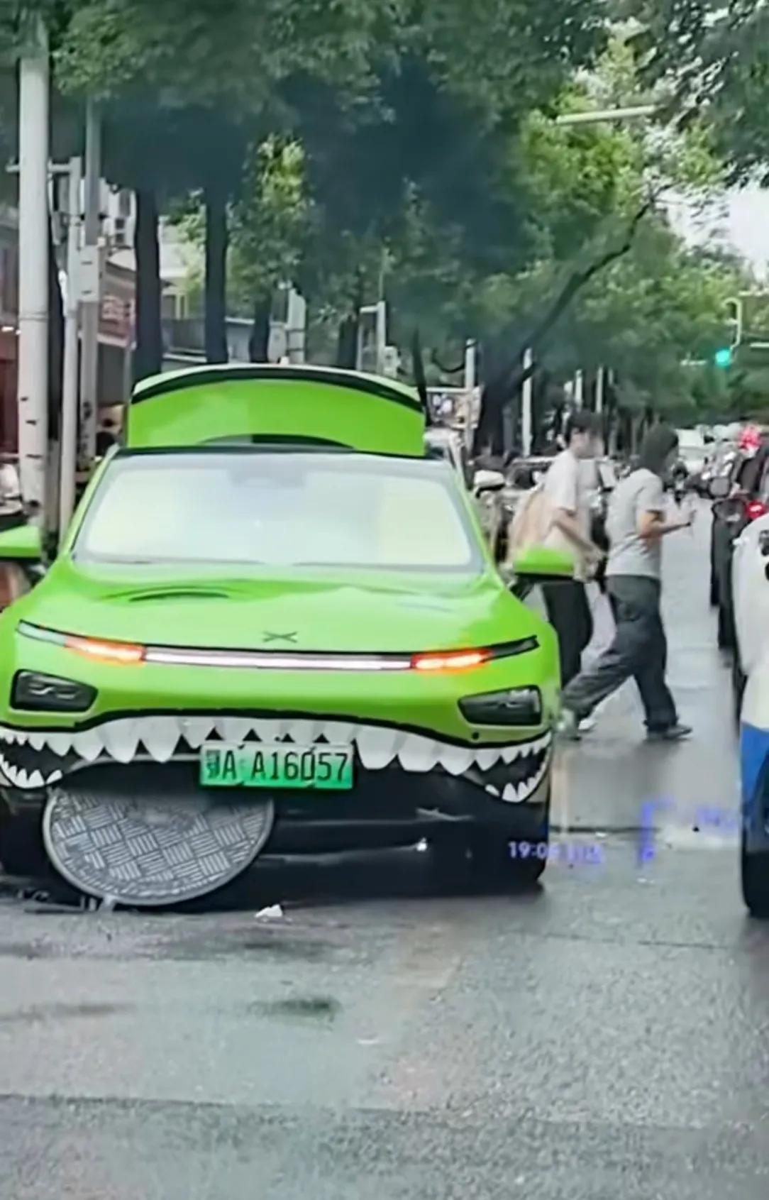 这画面也太巧了！小鹏贴了鲨鱼嘴车贴，刚好卡在掀开的井盖上，井盖露出来像被它一口咬