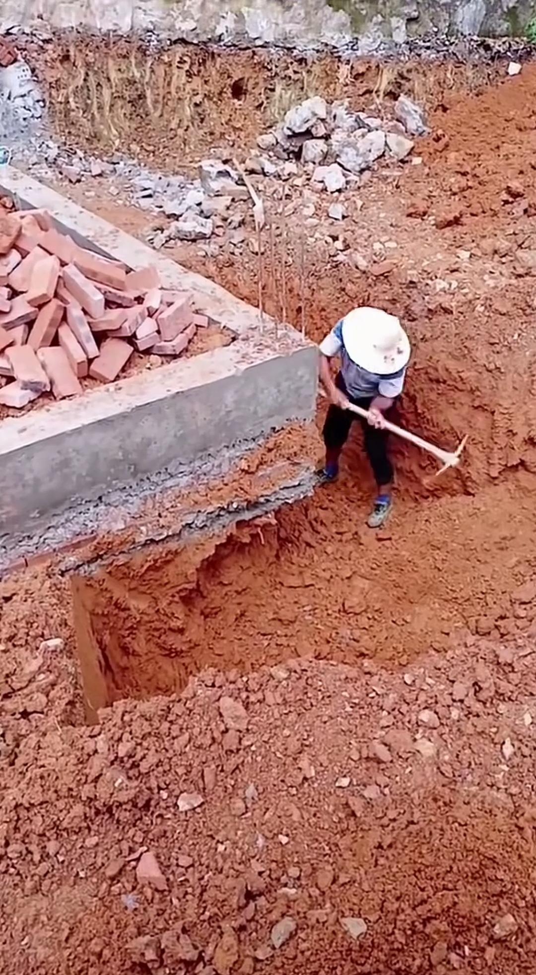 对着地基猛挖，是蓄意破坏还是加固墙基？谁见了这场景能不心惊？工人手持镐头对着地