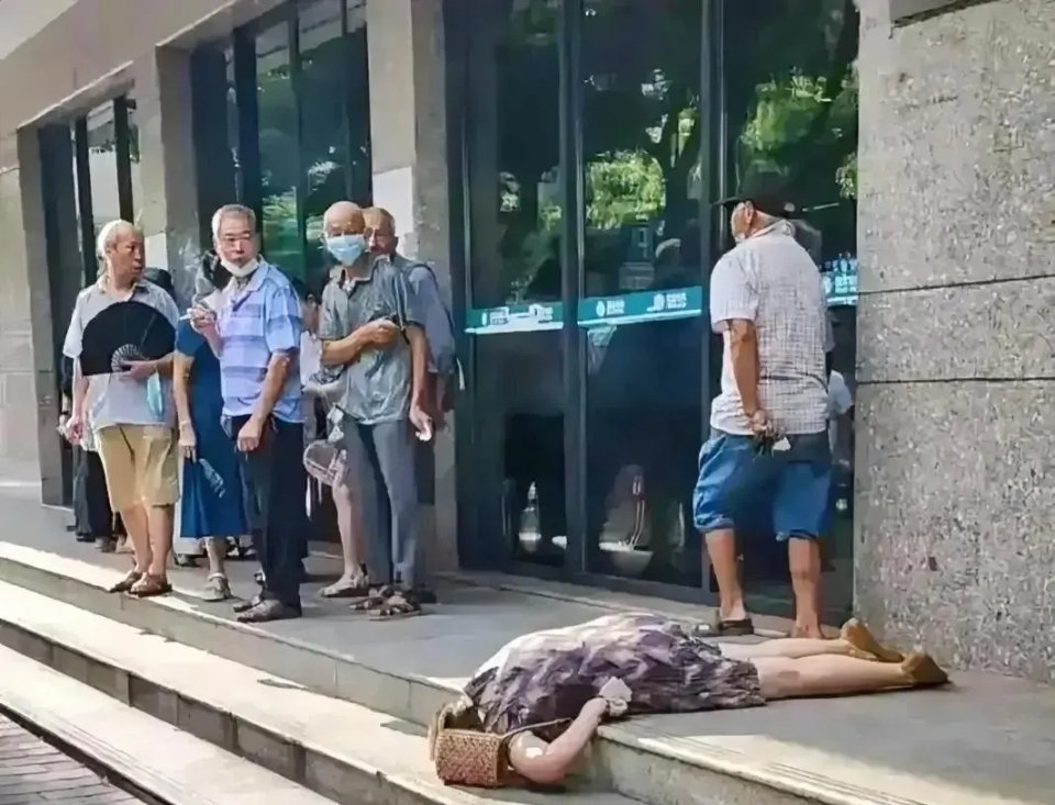 一家银行门口，一名中年女子突然倒地，群众围观着，就是没有人敢动。这个女子一直趴