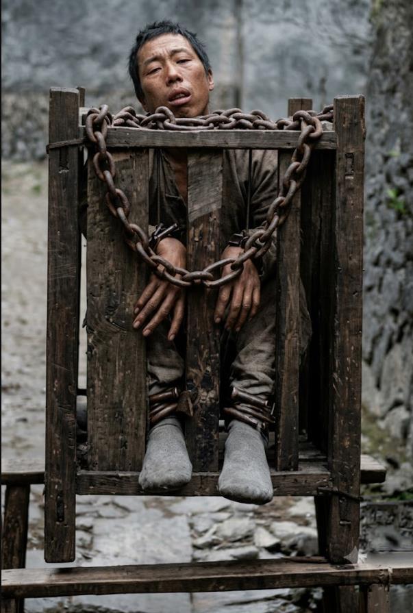 清末，一名被处以站笼（立枷）之刑的囚犯。囚犯被完全禁锢在特制的立式木笼中，脖颈
