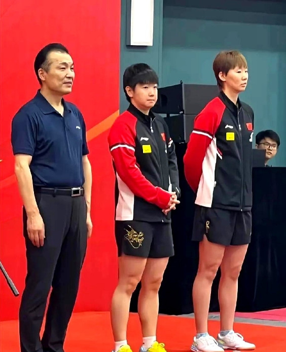 孙颖莎和王曼昱站在台上，莎莎双手交叉放在身前，曼昱则双手背在身后，一个朝前，一个