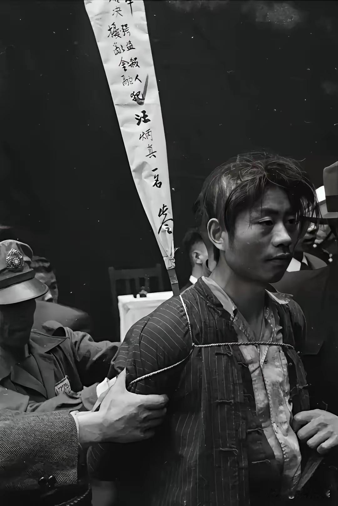 照片中的这个人，被五花大绑着押赴刑场，脖子后面上插着一个白色的招子，上面好像是写