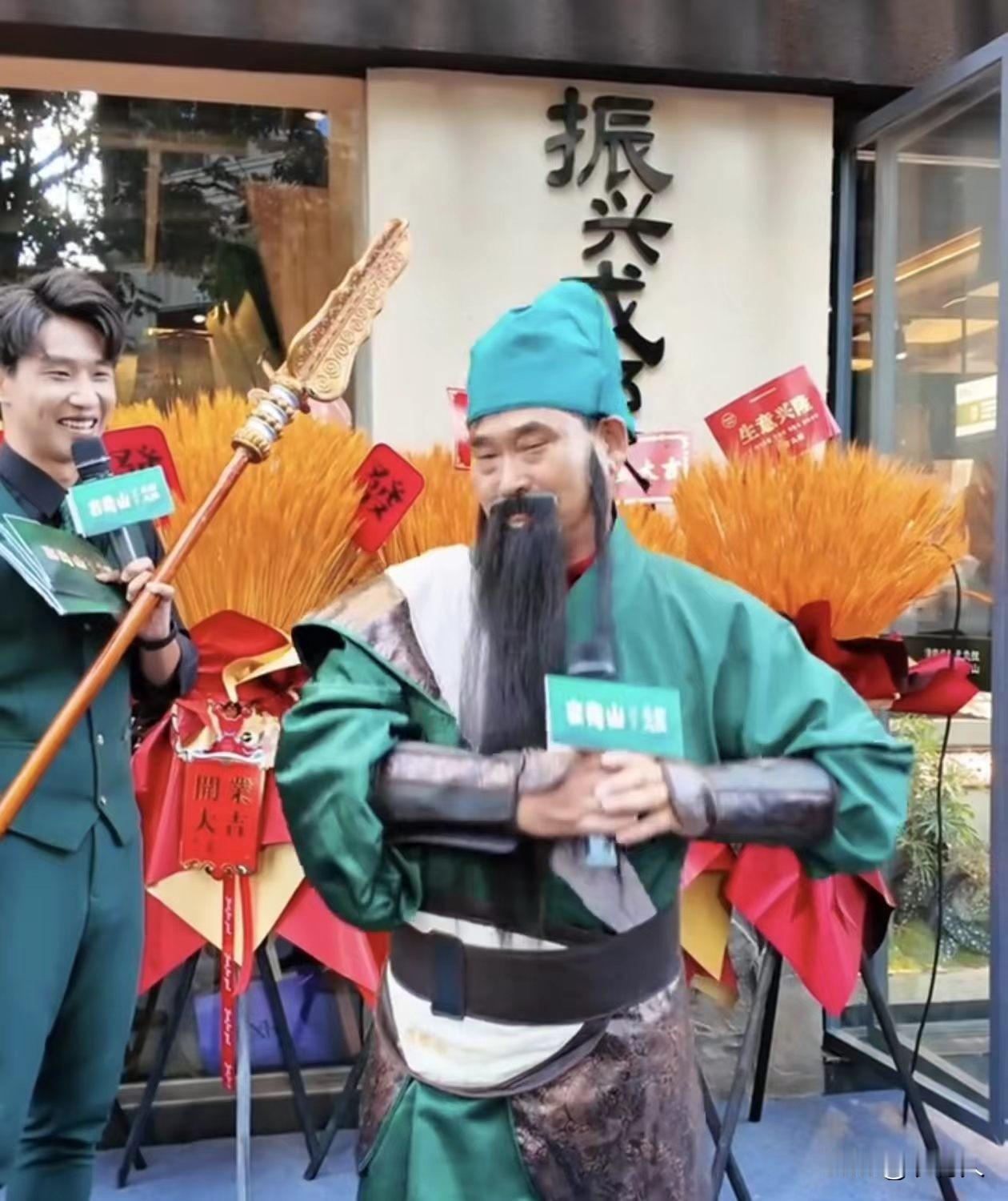 朱之文参加开业活动，一身绿袍配上长胡须青龙刀。在门店开业现场和主持人互动，朱之文