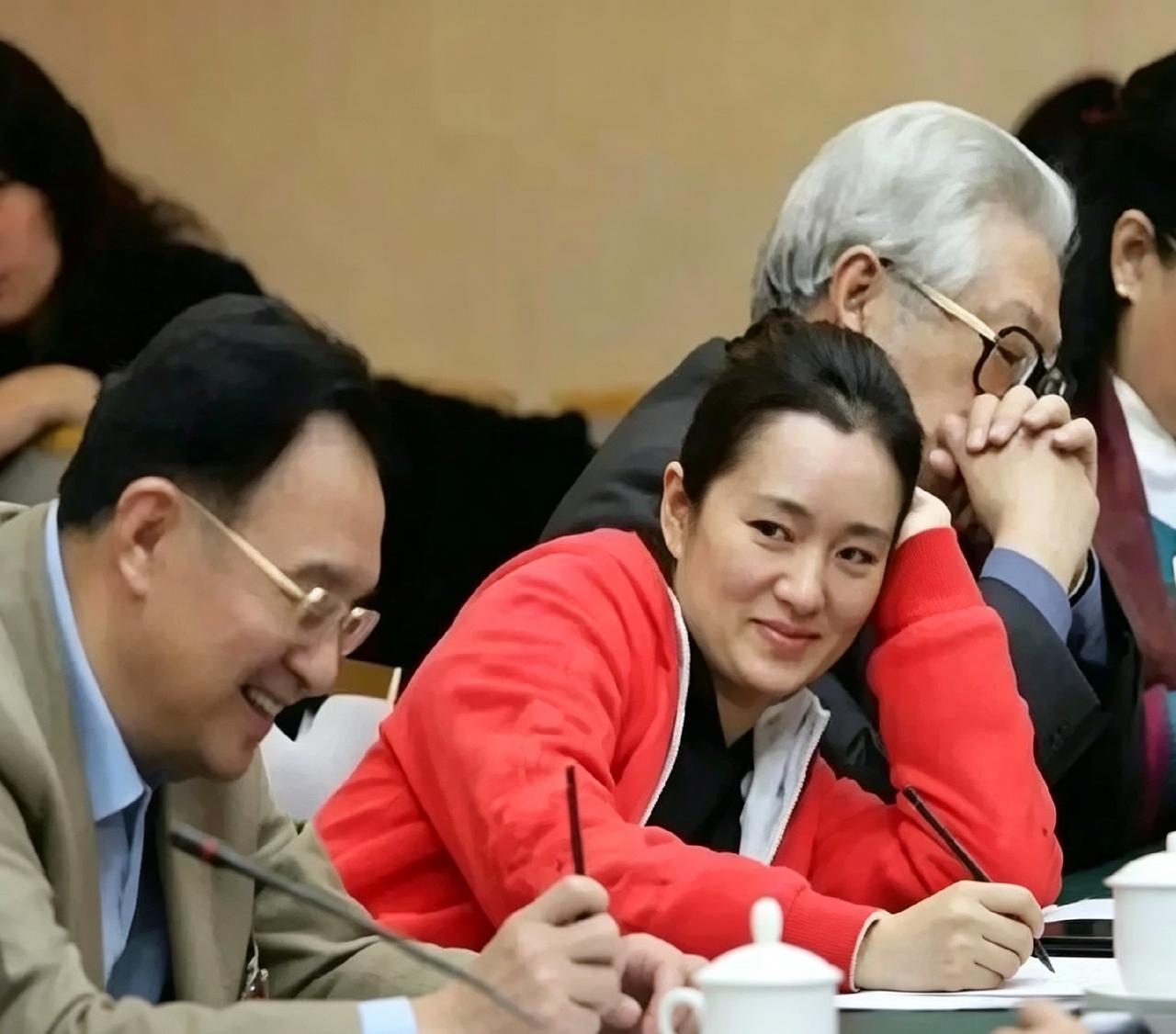 这张老照片里的巩俐真水灵。红衣裳一穿，托着腮帮子笑得特别甜，跟旁边人聊得正热乎。