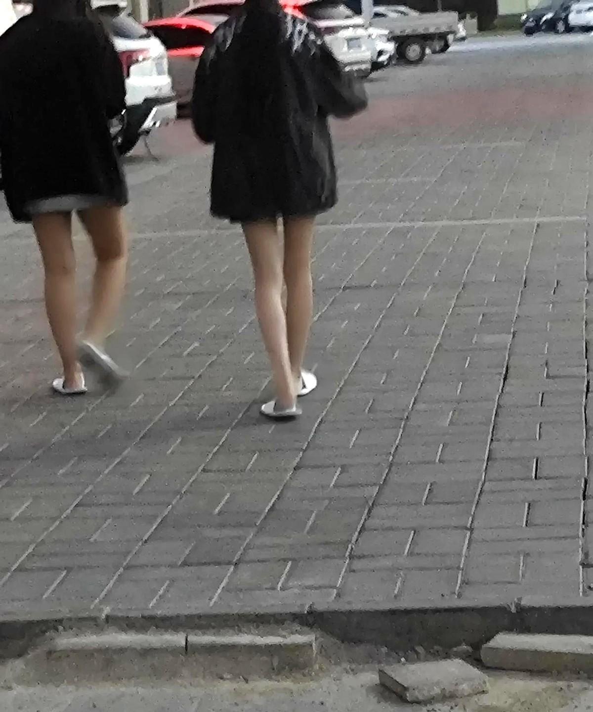 前面走着两个女孩子，穿着一双宾馆式拖鞋，上身穿着长长的夹克，基本上到臀了，下面露