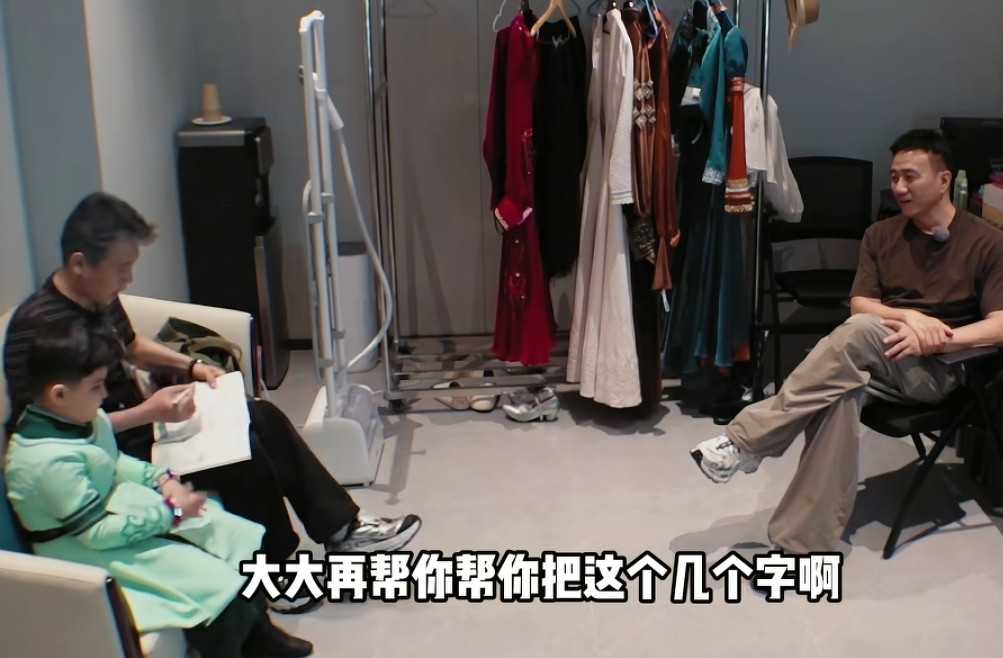 李乃文一个人坐沙发上教小孩儿学习，胡军一个人坐在凳子上一声不吭的看着，李乃文：“大大再帮你把这几个字