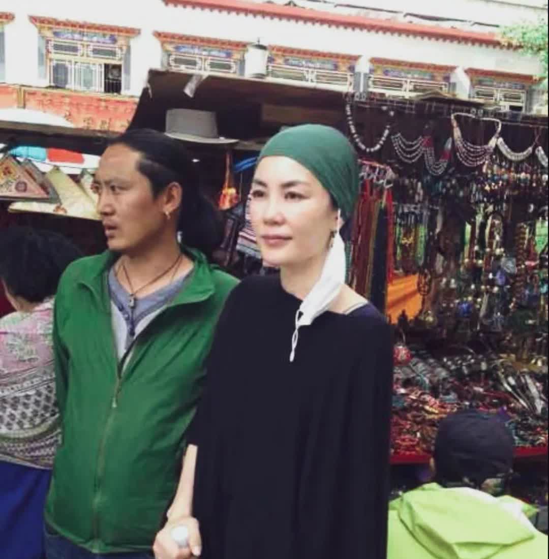 王菲西藏祈福头包绿色头巾，身穿黑色长袍。表情温和，慈眉善目。皮肤白皙胳膊纤细，面