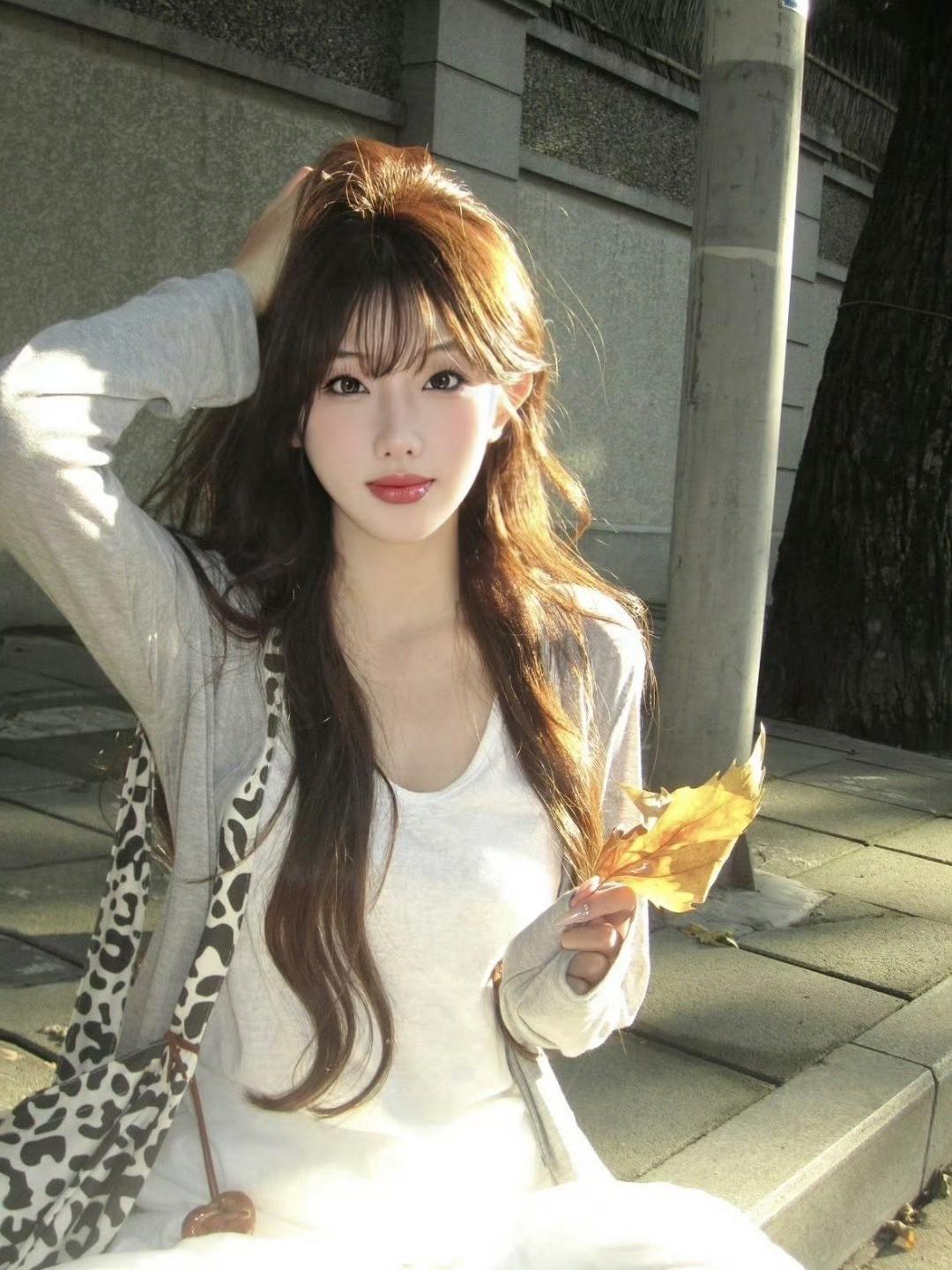 秋日暖阳下，少女轻抚发丝，手持落叶，唯美瞬间定格。