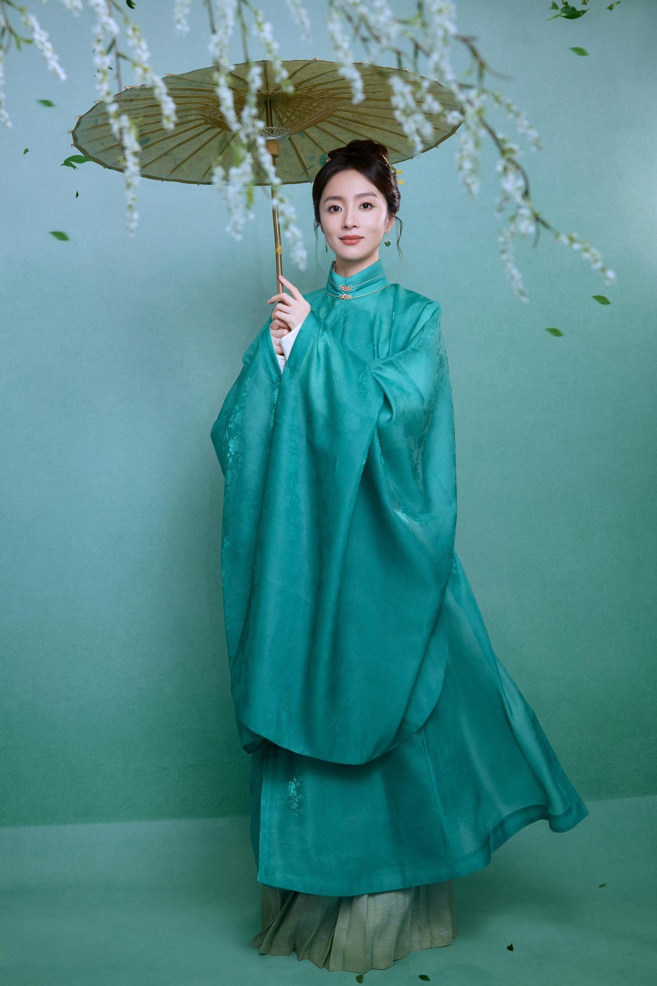胡冰卿身着明制风格的青绿服饰，手持一把油纸伞，背景有白色花枝与飘落的绿叶，整体营