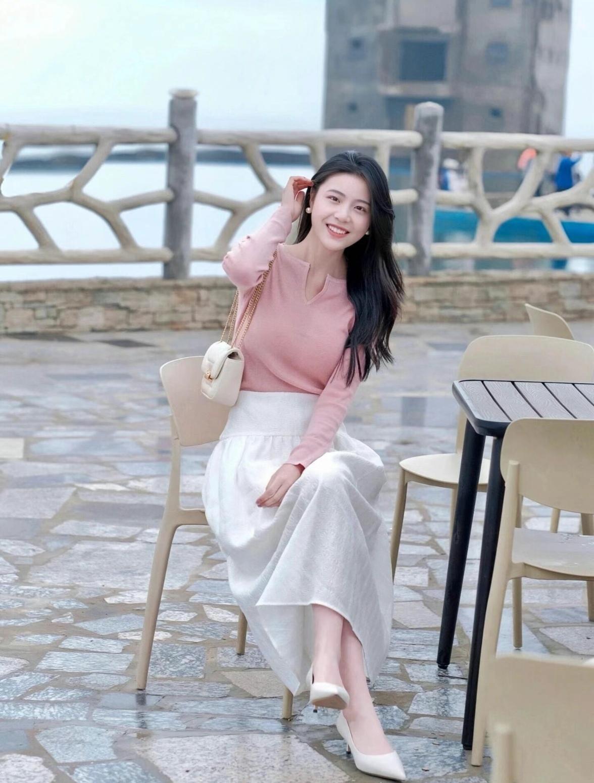 女孩在户外微笑，穿着粉色上衣和白色长裙。