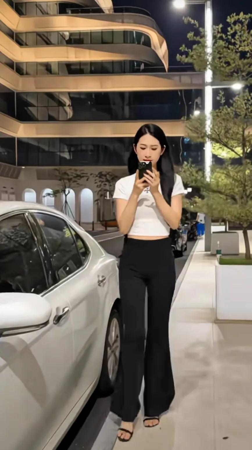 灯光下，美女静立如画。长发垂肩，乌黑如漆，她身后的楼层勾勒出圆润的弧形，素朴的白