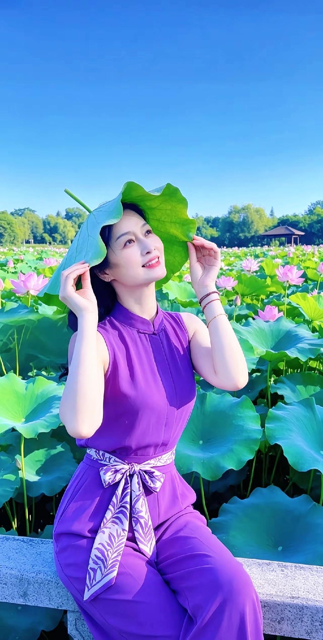 一个穿紫色衣服的人在荷花池边玩叶子。