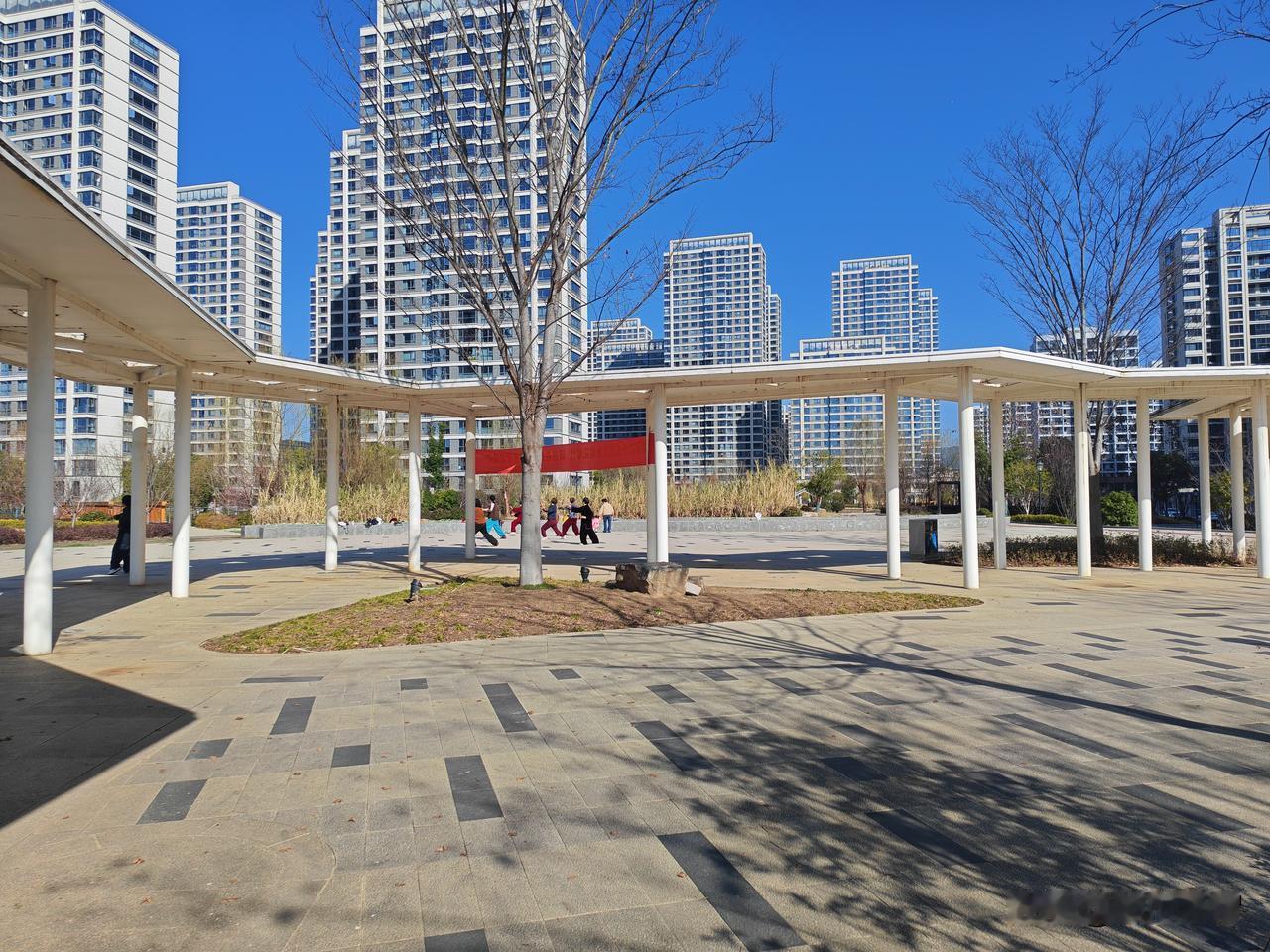 一群老太太在小广场打太极，一个一两岁的孩子好奇地走到他们中间，模仿着她们的动作。