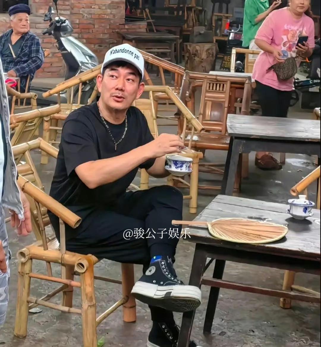 59岁任贤齐近日现身成都路边摊喝早茶，他穿着一套黑色休闲衣服，脚穿运动鞋，头顶白