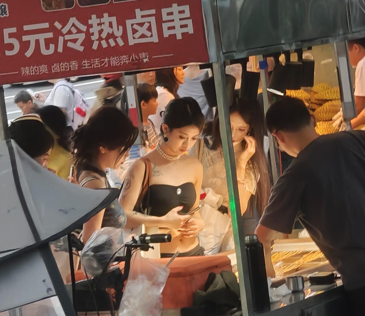 热闹街头，美女在卤串摊选购美食。