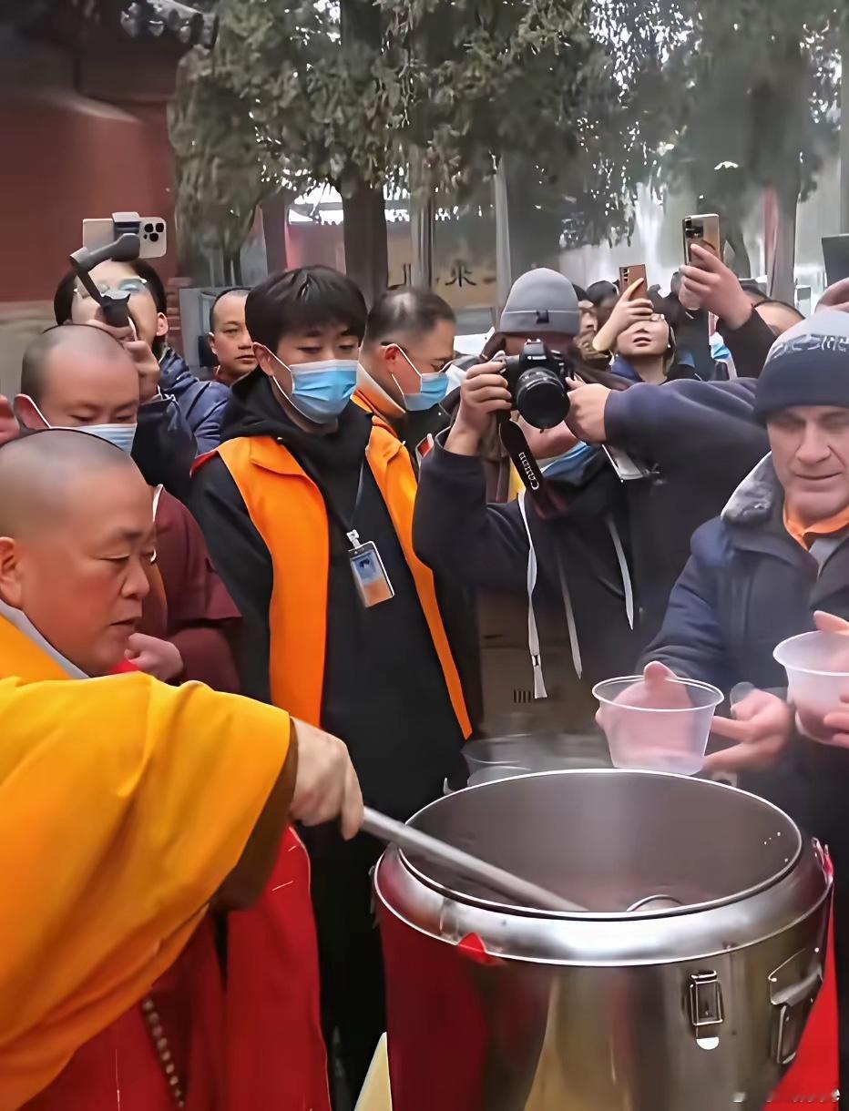 当年的释永信大师为香客们盛粥时的一幕，四周围满摄像机跟拍。