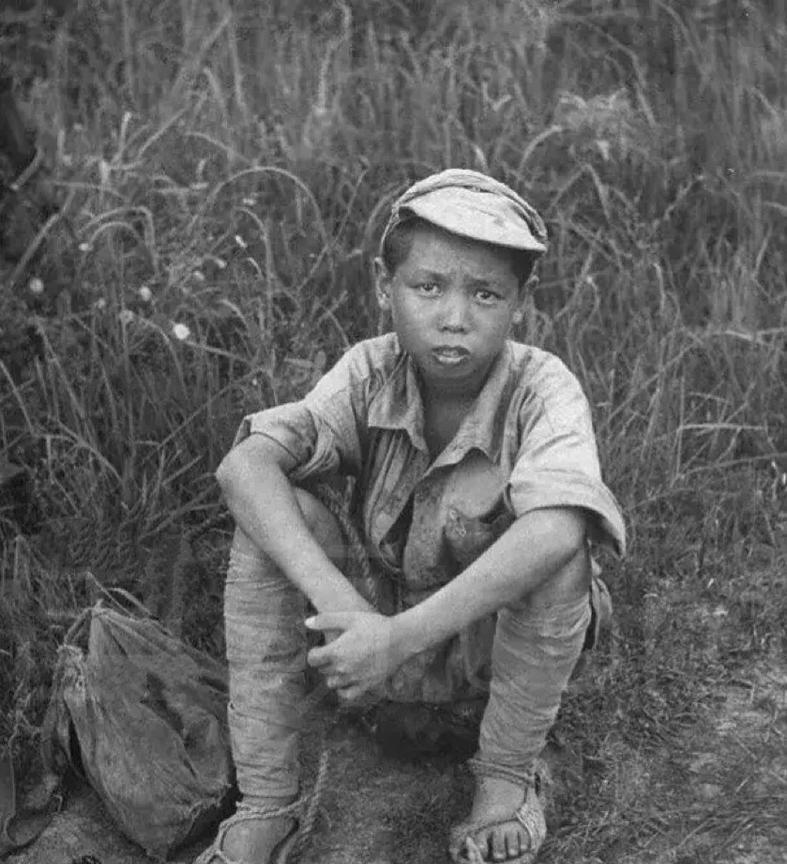 1940年，广西，一名穿着草鞋的少年兵坐在草丛边，穿着破旧而且明显大很多的军服，