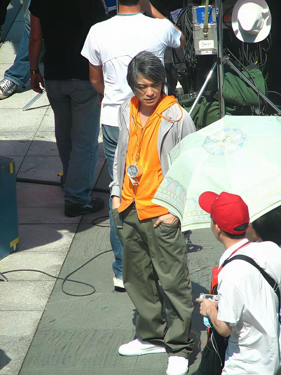 20年前的周星驰，站在那里与一名戴红色棒球帽的男子交谈。2006年的周星驰，