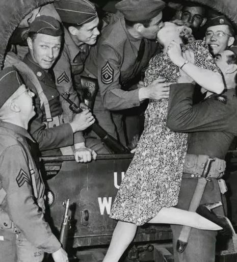 1940年，一名士兵举起一名年轻貌美的女人，将她送给卡车上的大兵，大兵见到女子不