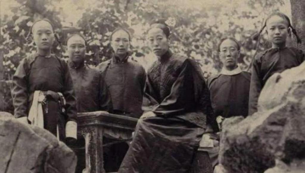 1912年秋，紫禁城御花园中，隆裕皇太后的一张老照片，她坐在一块石头上，一旁侍卫