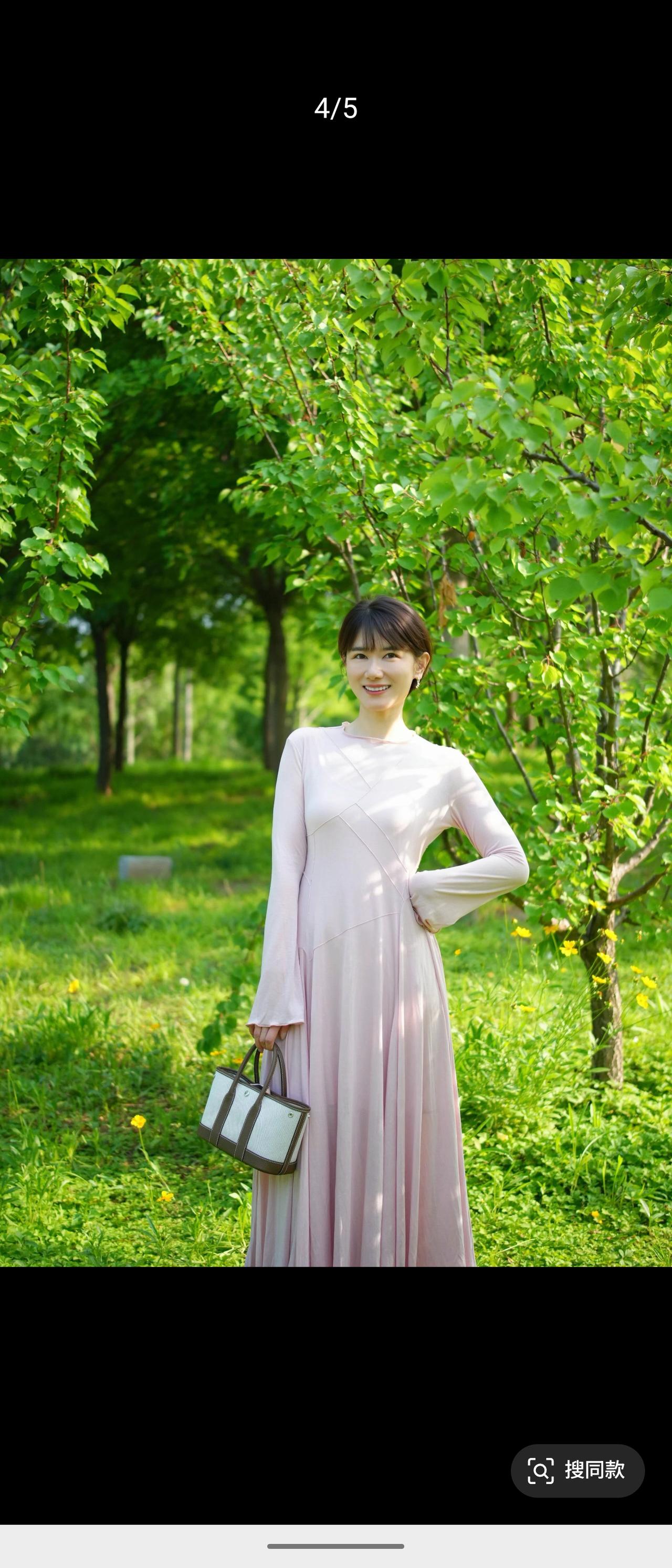 林间绿意盎然，浅粉长袖长裙温柔飘逸，贴合身形又尽显松弛。手提精致小包，短发清爽利