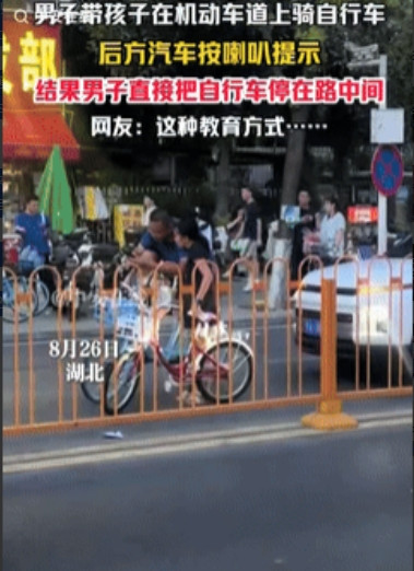 真把马路当自己家了！”湖北一男子带着孩子在机动车道骑自行车，后方汽车按喇叭提醒男