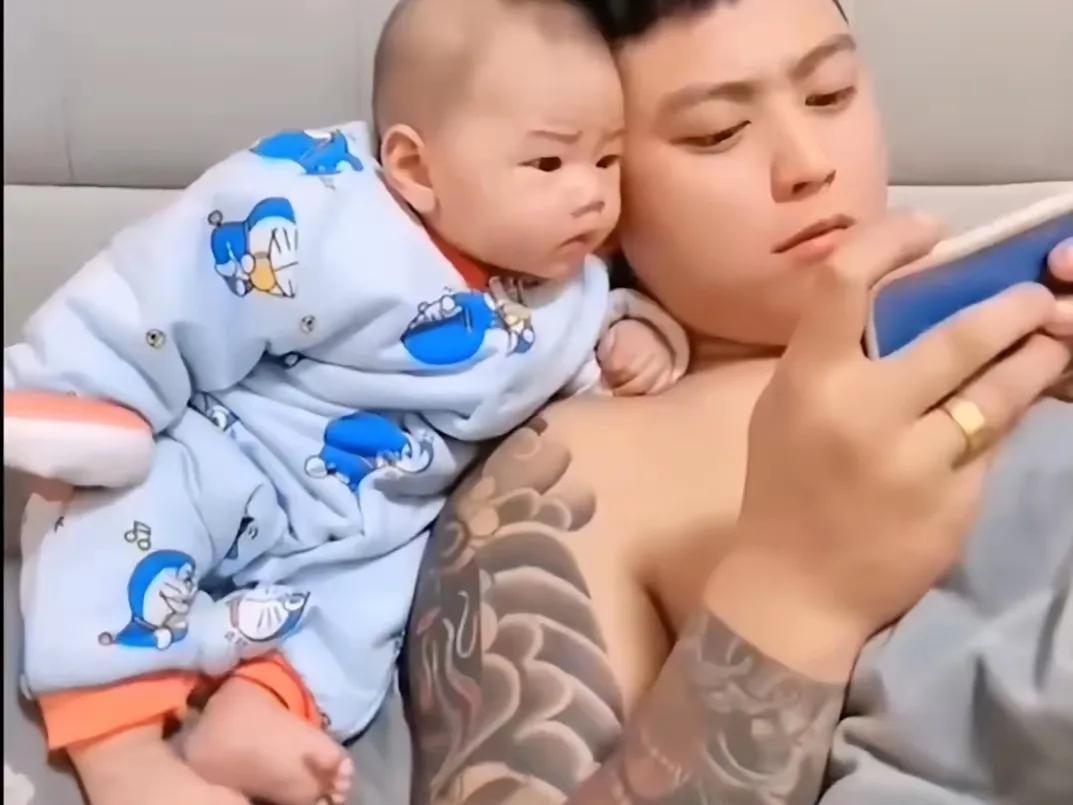 男子躺在床上看手机，儿子也依偎在他肩头伸着头瞅，爷俩看的很专注，眼睛都舍不得眨一
