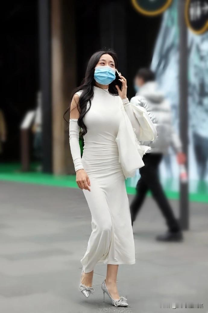 一位穿着白色套装的女士在街上走着，戴着口罩。
