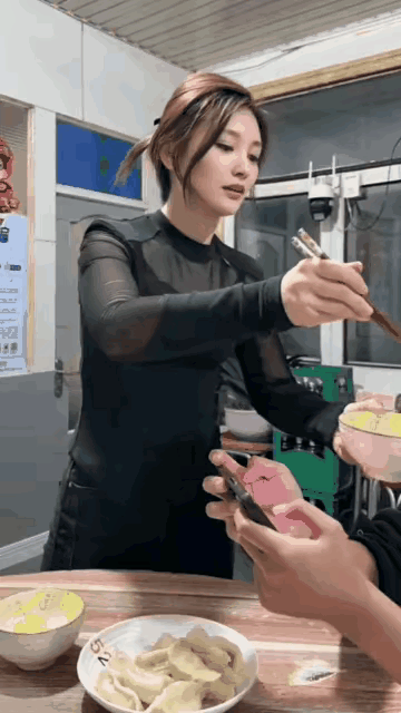 男子坐在饭桌边，还在忙着用手机打游戏，他的妻子端着碗给他喂饺子吃！小姨子在旁