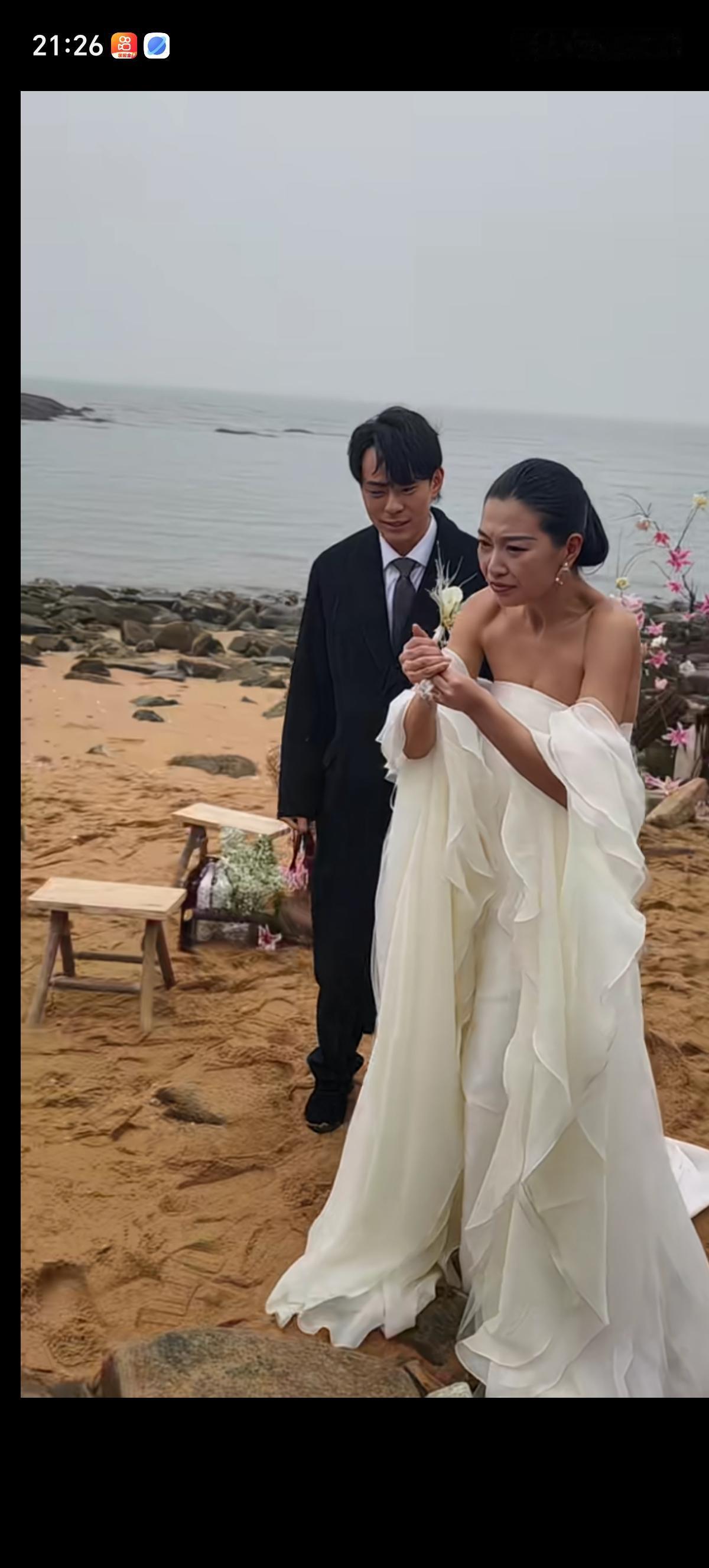 拍婚纱照的新娘冻的瑟瑟发抖，不停的搓着双手，新郎在旁边默默的看着。在旁边的小姐姐