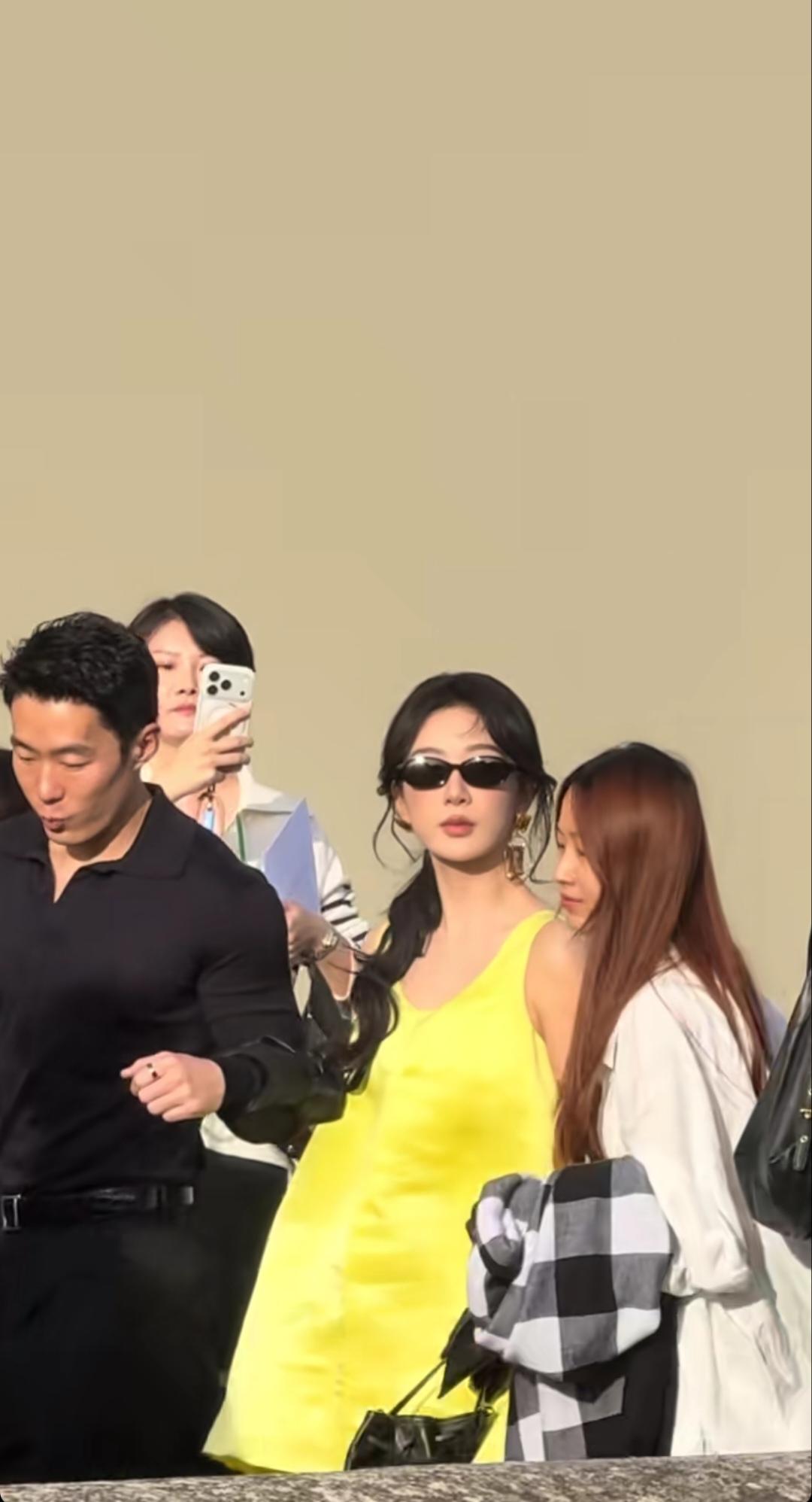 杨紫现身巴黎时装周，黄色背心款裙子，戴着小墨镜，黑手套，她一手搭在身边男士的小臂
