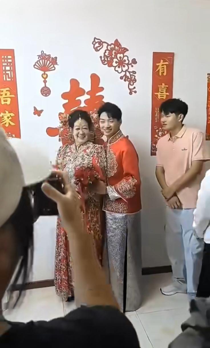 一场特殊的婚礼，小伙子迎娶年长阿姨。两人笑容满面从容拍照，一旁围观的宾客表情耐