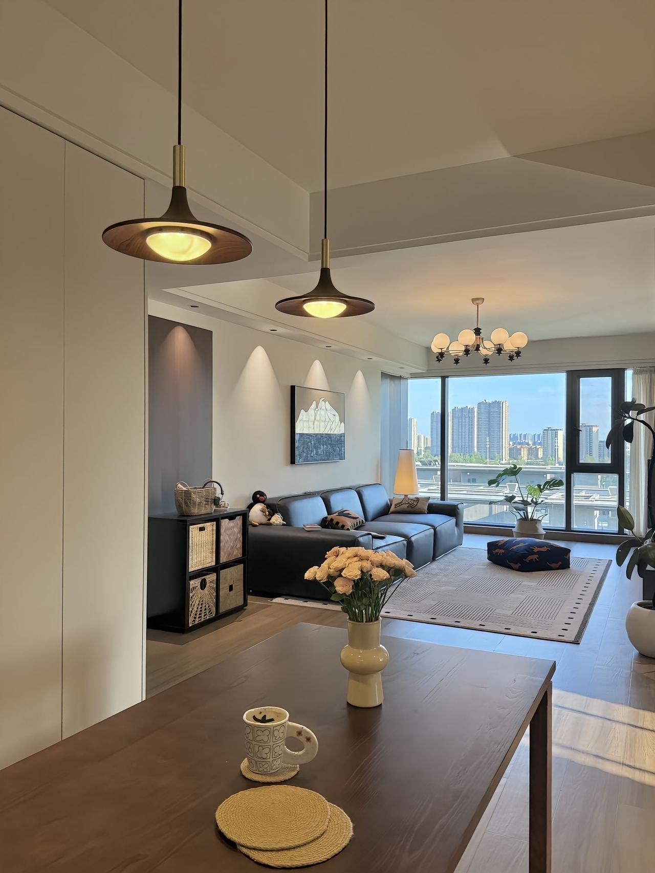 这是一处现代风格的居室,空间通透明亮。餐厅区域的深木色餐桌摆放着插有浅粉色花朵的