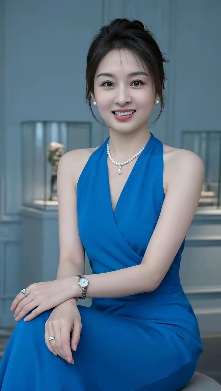这位女士穿着蓝色连衣裙，微笑着坐在那里，珠宝闪耀，气质满分。