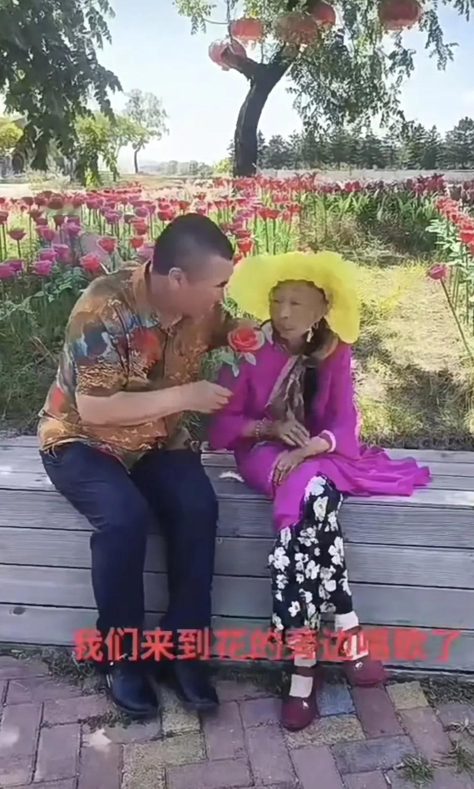 87岁的马玉琴打扮得年轻小媳妇似的，来到花团锦簇的公园里，和小丈夫李玉成唱起了歌
