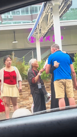 一个老外正在街头和一名中国女子约会。在他们旁边竟然还站着一位卖花的老奶奶？老