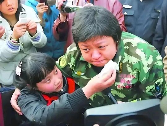 废墟上的温柔救灾现场，尘土还没散尽，韩红穿着迷彩服，蹲在孩子面前。她手里攥着