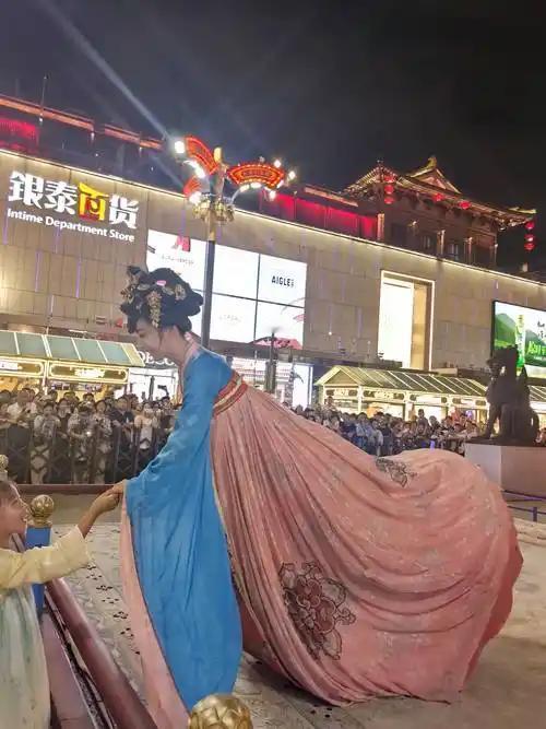 暮色漫过西安城墙时，大唐不夜城的灯又亮了。人群里忽然一阵欢呼——冯佳晨提着唐制裙