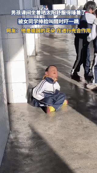 课间时分，小男孩蹲在走廊里晒着太阳，舒服得直接闭上眼睛睡了过去。一旁的女同学看到