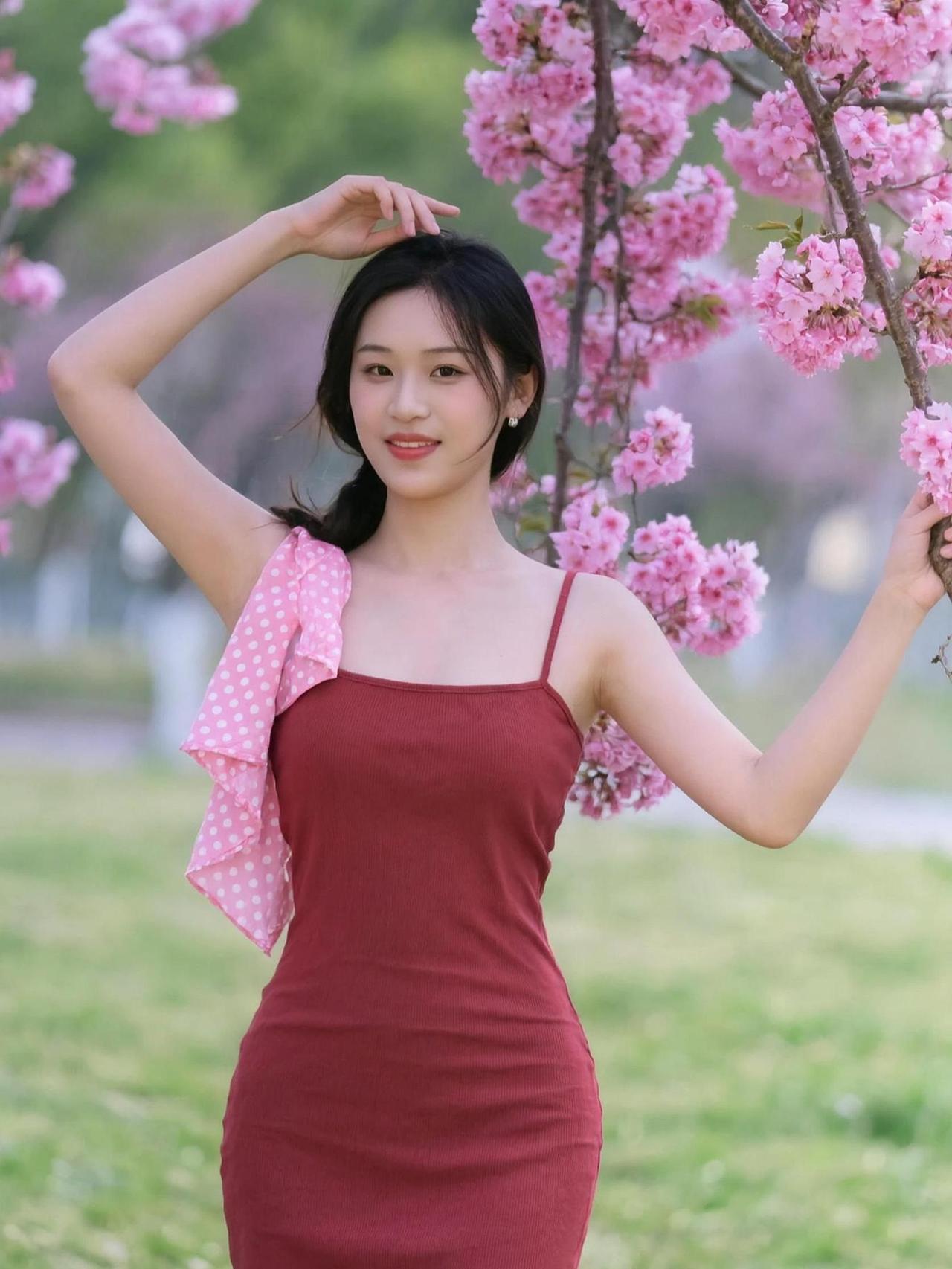 在樱花树下，微风轻拂，花瓣如雨般飘落，仿佛时间也在此刻静止。一袭红裙，映衬着春日